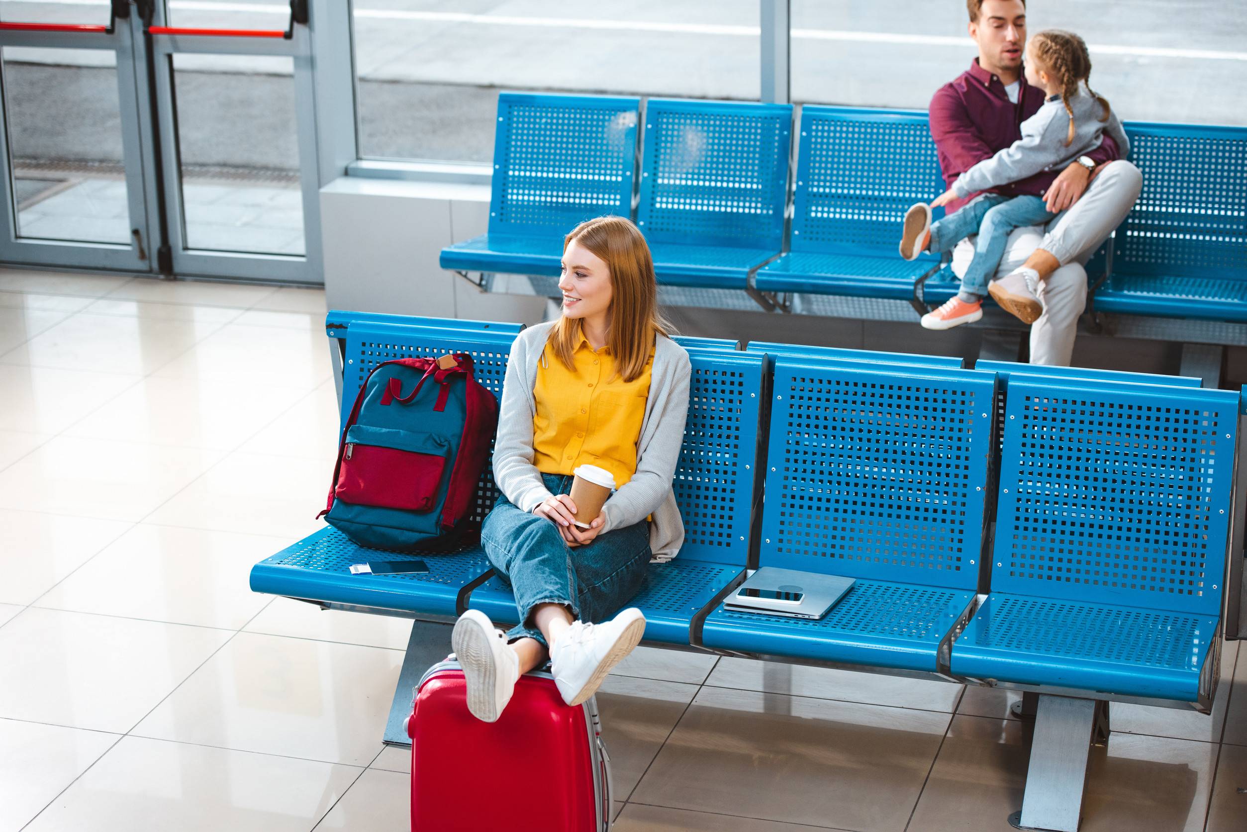 Smiling Woman Holding Paper Cup In Airport Near Backpack Smiling Woman Holding Paper Cup In Airport Near Backpack